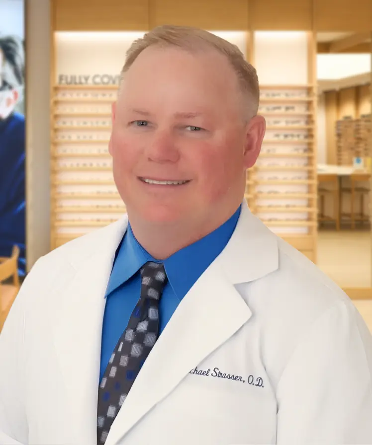 Dr. Michael Strasser wearing a white coat and smiling, stands inside an eyewear store.