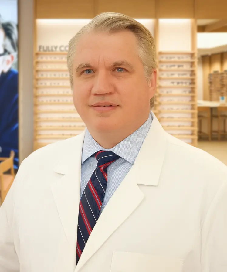 Dr. Kevin Harte wearing a white coat and smiling, stands inside an eyewear store.