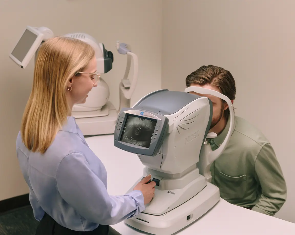 An eye technician performs a vision test on a man using an advanced eye examination machine in a clinical setting.
