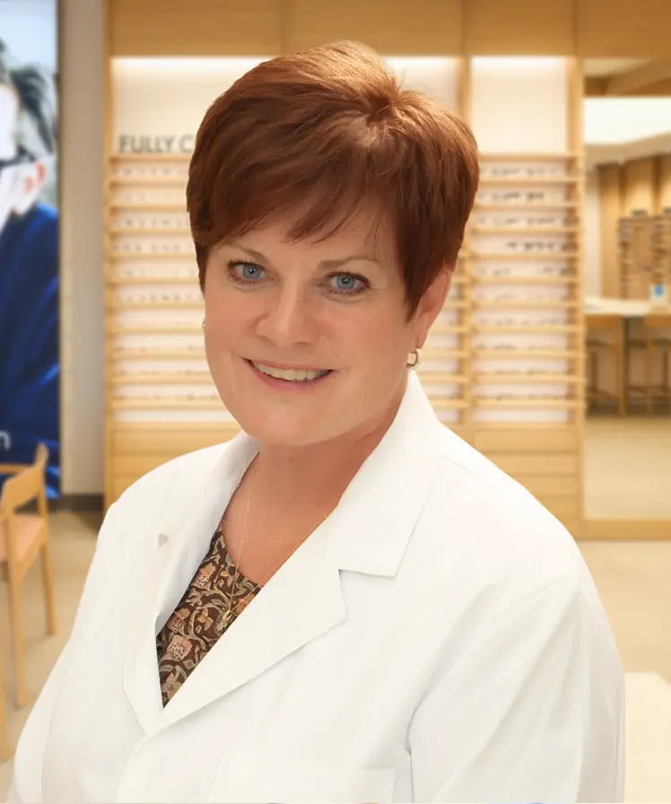 Dr. Kathryn Wilson wearing a white coat and smiling, stands inside an eyewear store.