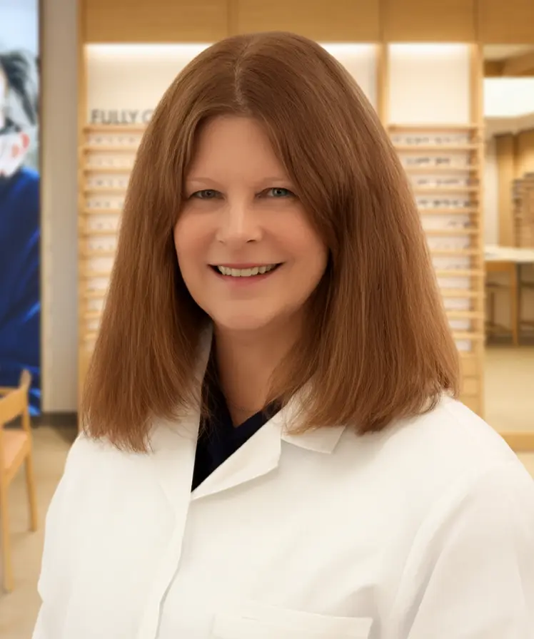 Dr. Lori Wassmann wearing a white coat and smiling, stands inside an eyewear store.