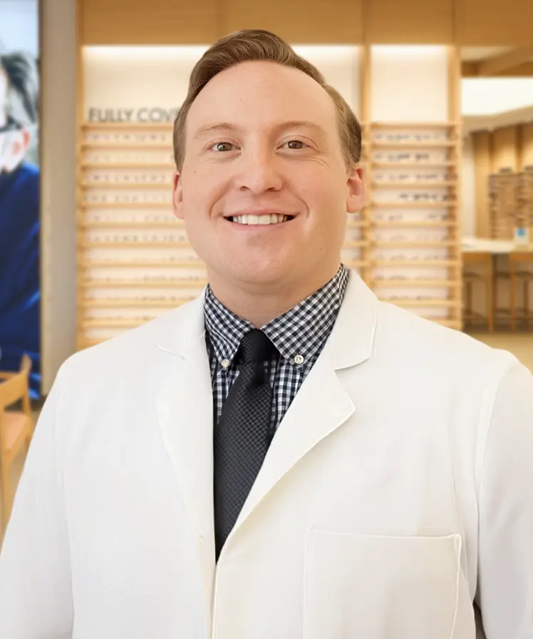 Dr. James Adams wearing a white coat and smiling, stands inside an eyewear store.