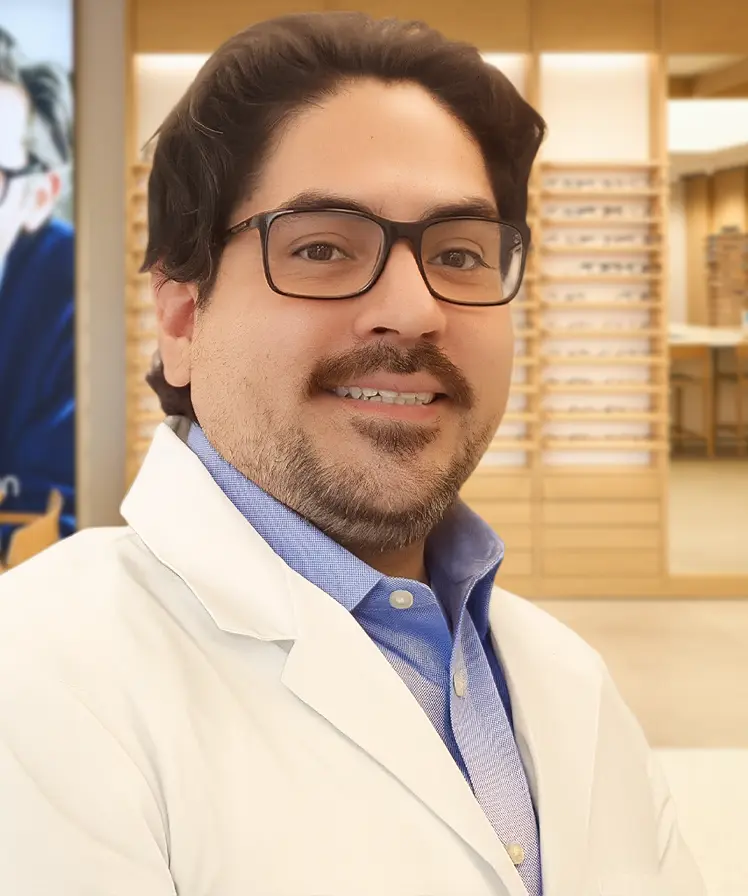 Dr. Giacomo Cilliani wearing a white coat and smiling, stands inside an eyewear store.